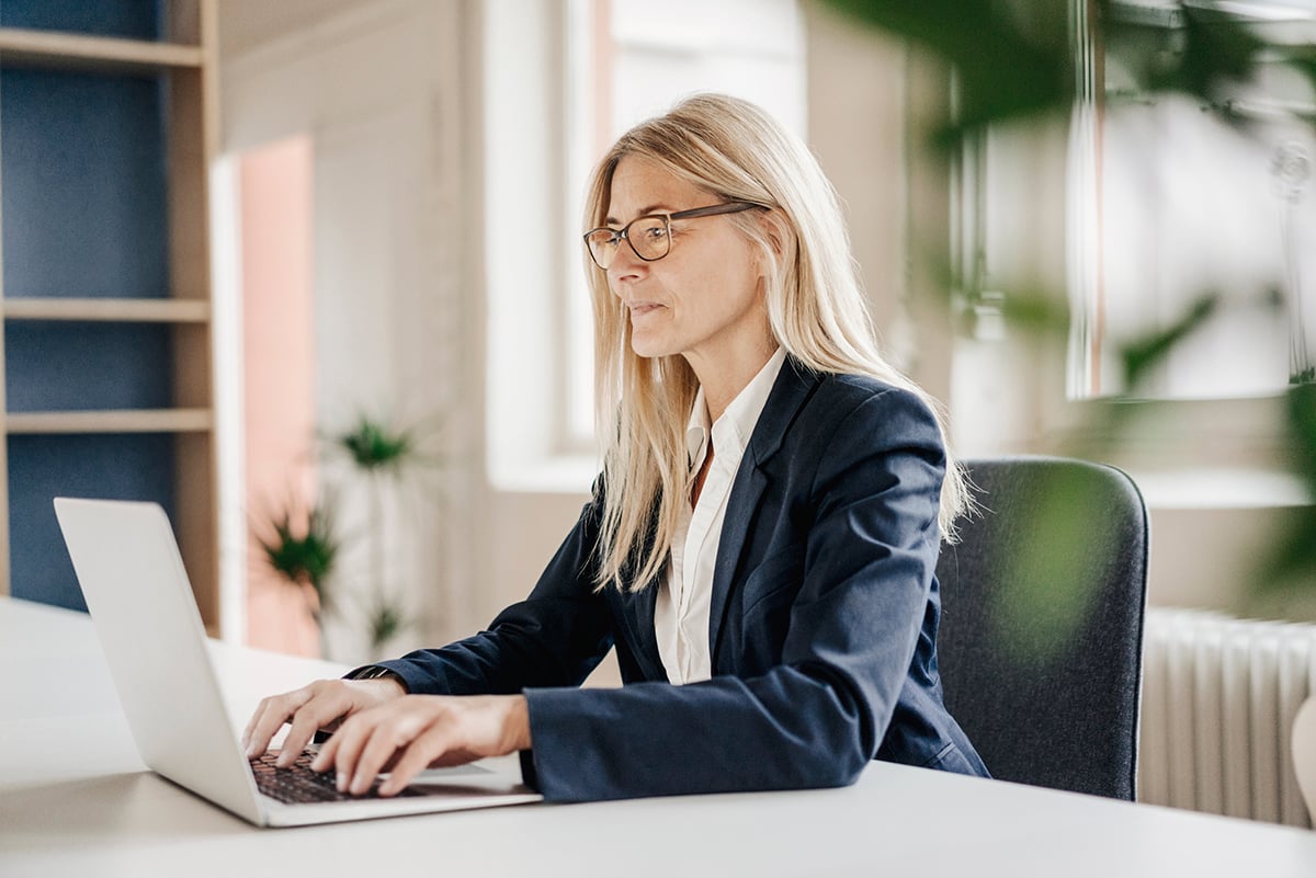 Blonde lady with glasses working on a laptop